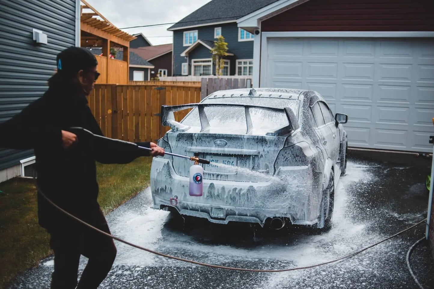 Man spraying soap off of a car with a pressure washer.