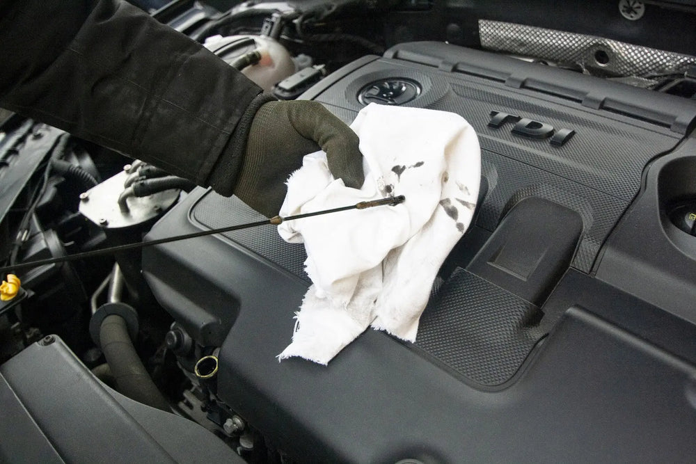 
              Man using a dipstick to check the oil level of a car.