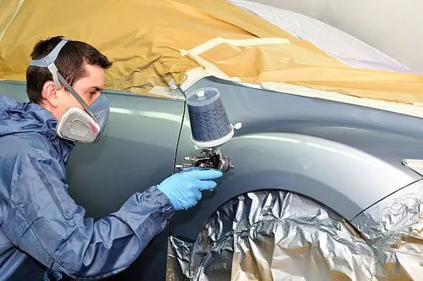 
              Man using a spray gun to apply paint to a silver cars front fender.