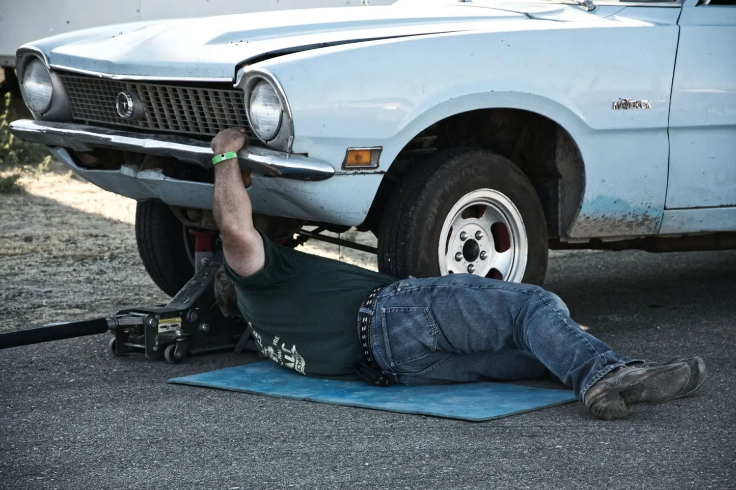 
              Man working to remove oil drain plug from a blue vintage car.