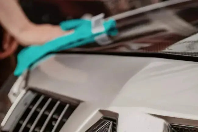 Person removing car wax with a blue microfiber cloth.